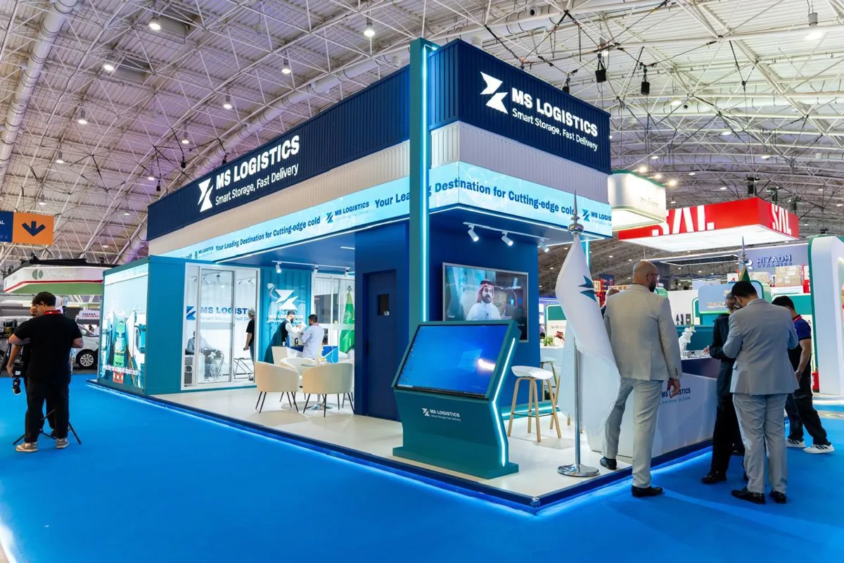 The MS Logistics stand in the exhibition hall, with its illuminated fascia, a touch-screen kiosk and the meeting area behind glass.